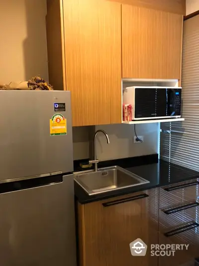 Modern kitchen with sleek cabinetry, stainless steel fridge, and microwave in compact design.