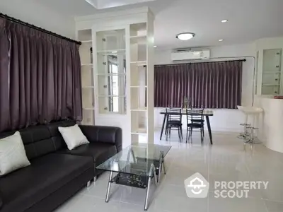 Modern living room with sleek black sofa and glass coffee table, featuring elegant curtains and dining area.