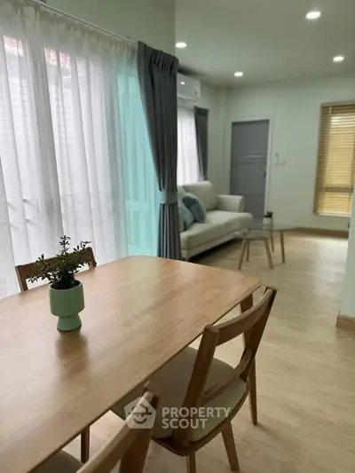 Modern living room with wooden dining table, cozy sofa, and elegant curtains in a bright, airy space.