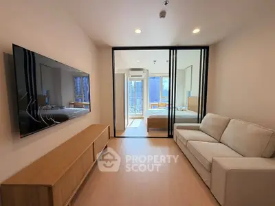 Modern living room with sleek TV, cozy sofa, and glass partition leading to a bright bedroom with city views.