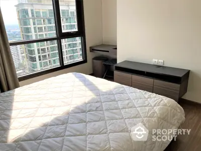 Sunlit modern bedroom with large windows offering a city view, featuring a cozy bed and sleek furniture, ideal for urban living.