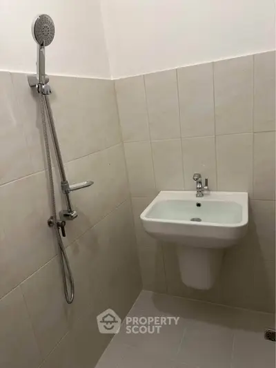 Minimalist bathroom with wall-mounted sink and showerhead in tiled space.
