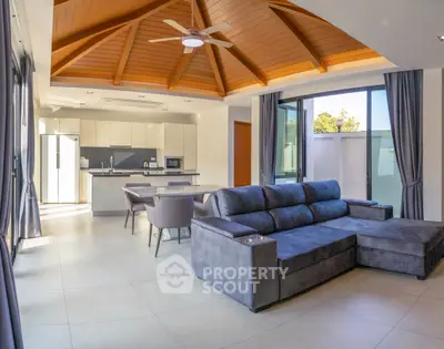 Spacious modern living room with vaulted ceiling and open kitchen layout, featuring elegant furniture and ample natural light.