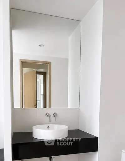 Modern minimalist bathroom with sleek black countertop and round white basin.