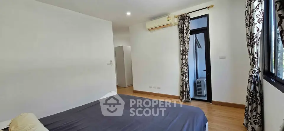 Spacious bedroom with modern decor and natural light, featuring elegant curtains and wooden flooring.