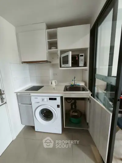 Compact kitchen with modern appliances including washing machine and microwave, ideal for urban living.