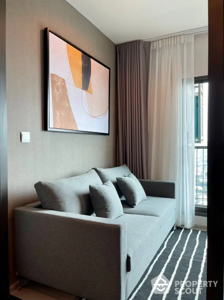 Chic modern living room with plush grey sofa, elegant art piece, and floor-to-ceiling windows offering ample natural light.