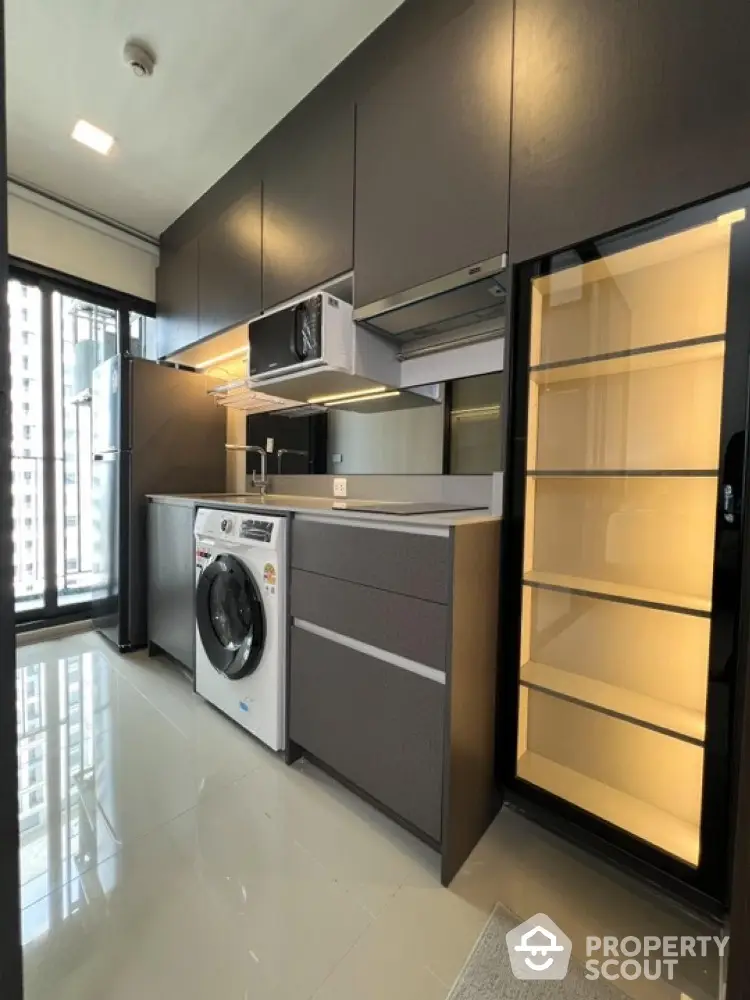 Modern kitchen with sleek cabinets, washing machine, and large fridge in a high-rise apartment.