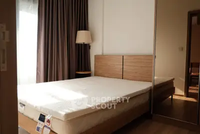 Spacious bedroom with natural light, wooden bed frame, and mirrored wardrobe in modern apartment.