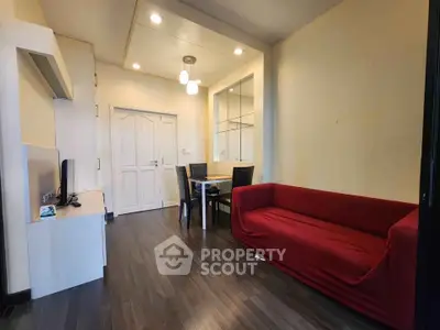 Modern living room with red sofa and dining area, featuring sleek wooden flooring and ambient lighting.