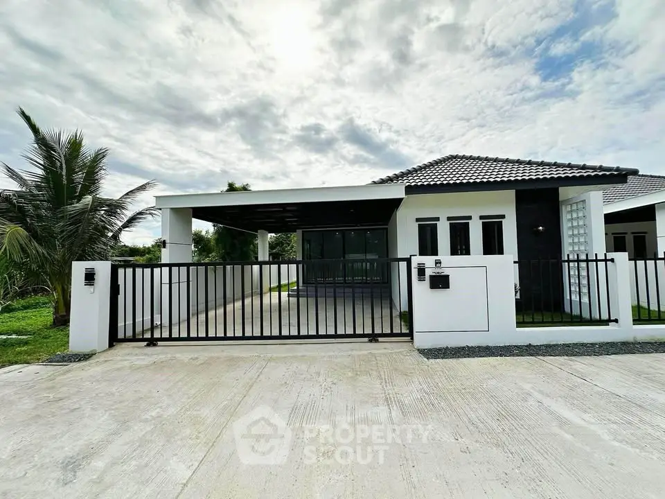Modern single-story house with sleek design and gated entrance under a cloudy sky.