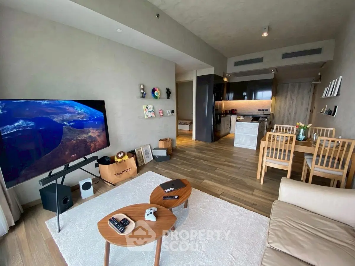 Modern living room with open kitchen, featuring stylish furniture and large TV, perfect for entertaining.