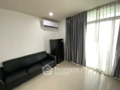 Modern living room with black leather sofa and air conditioning, featuring large window with curtains.