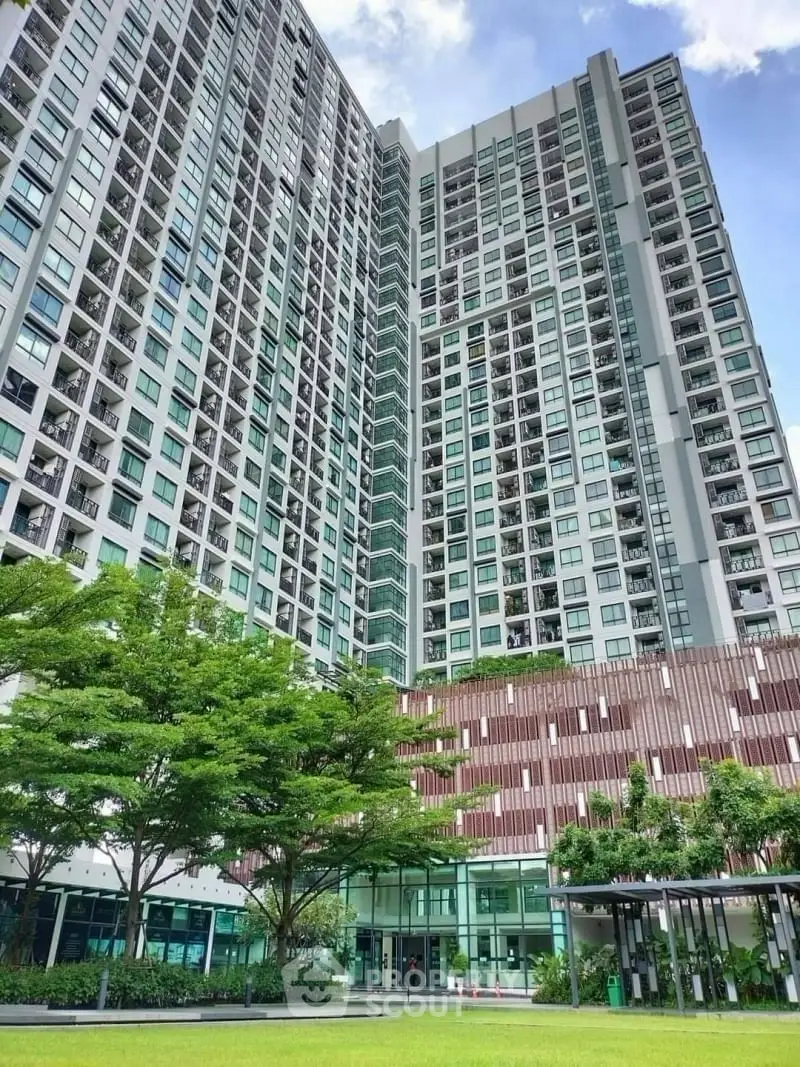 Modern high-rise residential building with lush green surroundings and clear blue sky.