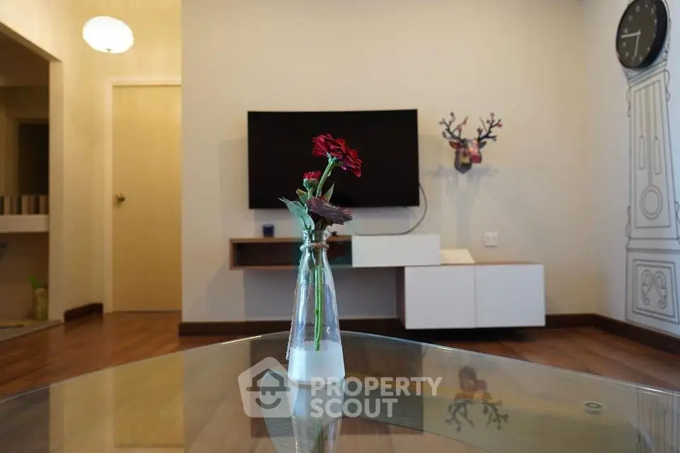 Modern living room with stylish decor and wall-mounted TV, featuring a glass table centerpiece.