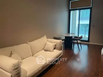Spacious living room with modern sofa and dining area, featuring large window for natural light.