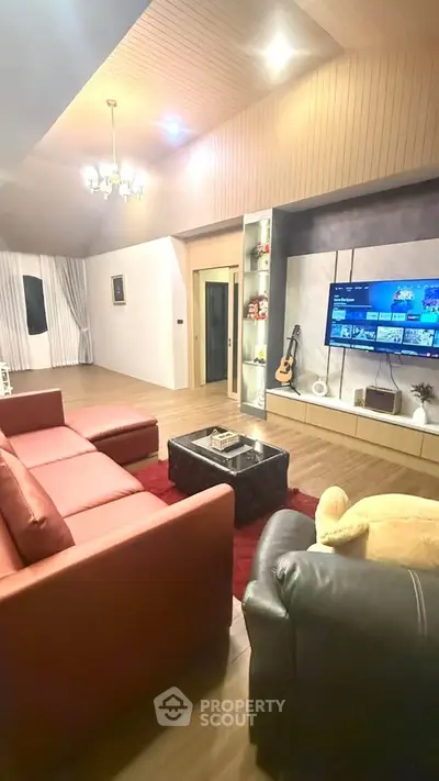 Spacious living room with modern decor, featuring a large TV, cozy seating, and elegant lighting.