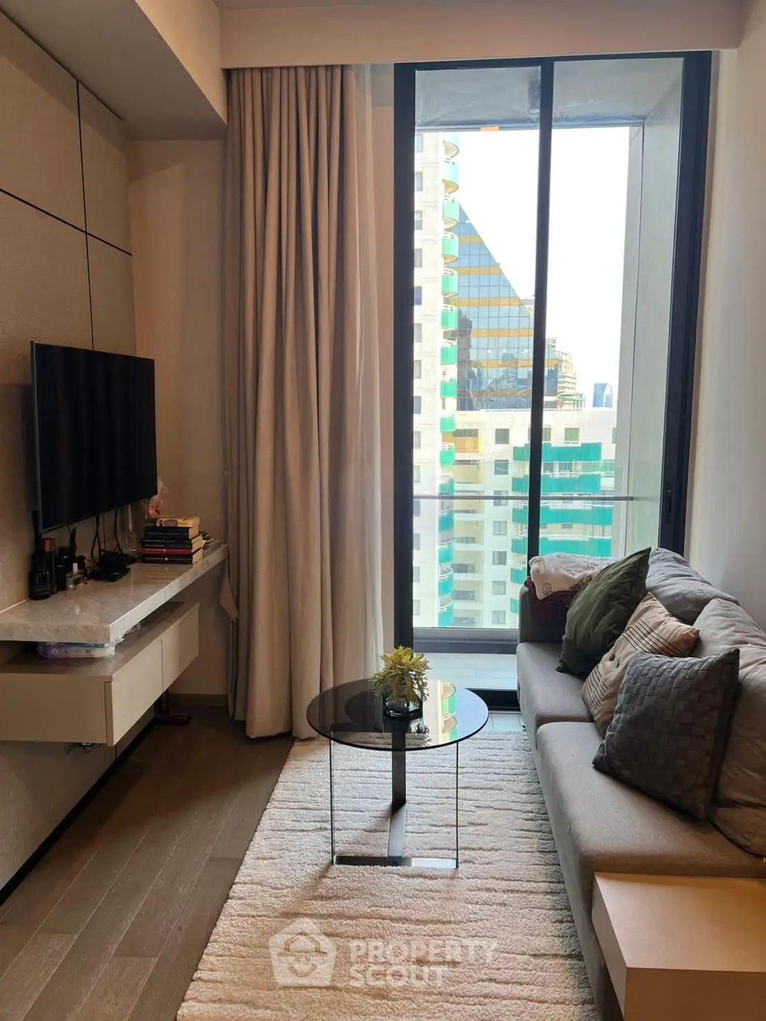 Modern living room with large window and city view, featuring cozy sofa and sleek TV setup.