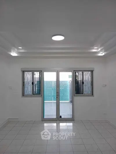Spacious tiled room with large windows and sliding glass doors leading to a balcony.