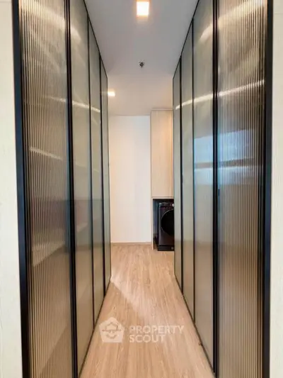 Modern hallway with sleek sliding doors and wood flooring leading to a laundry area with a washing machine.