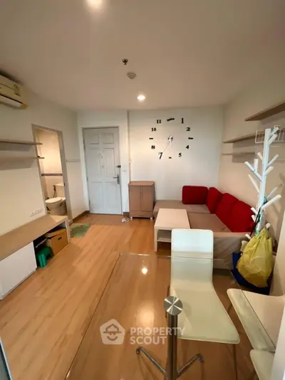 Cozy living room with modern decor and wall clock, featuring wooden flooring and red sofa accents.