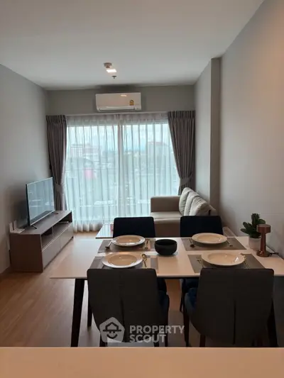 Modern living room with dining area, featuring sleek furniture and large window for natural light.