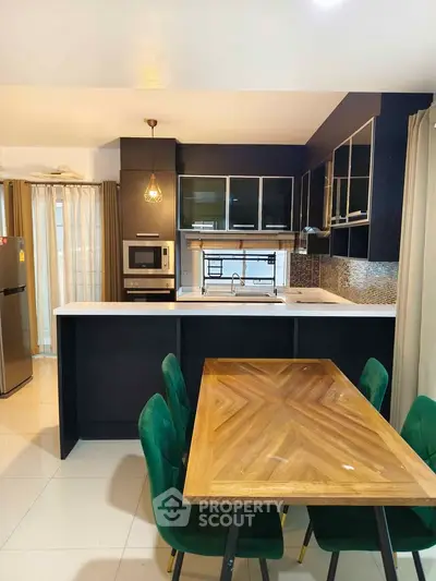 Modern kitchen with sleek black cabinetry, built-in oven, and elegant dining area with green chairs.