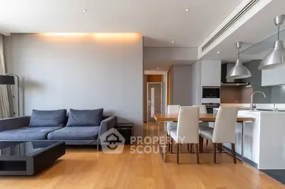 Modern open-plan living room with sleek kitchen and dining area, featuring stylish furniture and wooden flooring.