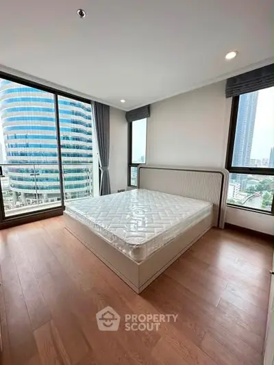 Spacious bedroom with large windows offering stunning city views in a modern high-rise apartment.