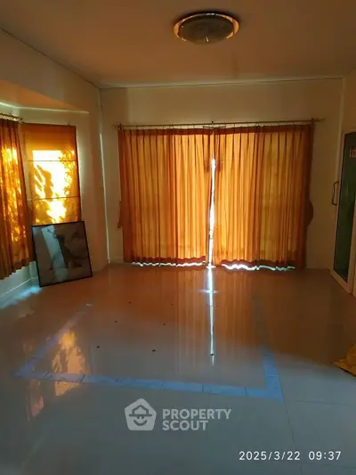 Spacious living room with large windows and warm curtains, ideal for natural light.