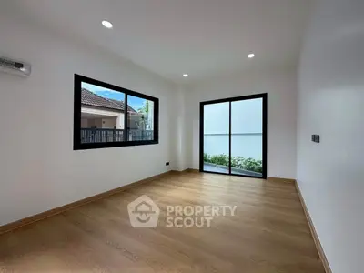 Spacious empty room with wooden flooring and large windows, perfect for customization.