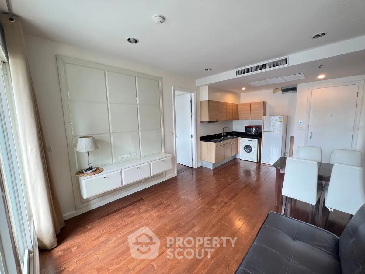 Modern living room with wooden flooring, open kitchen, and dining area in a stylish apartment.