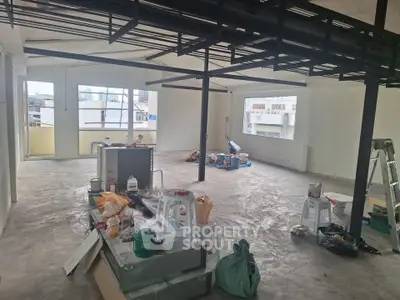 Spacious industrial-style loft under renovation with large windows and open layout.