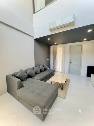 Modern living room with sleek gray sofa and air conditioning, featuring minimalist design and natural light.