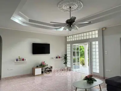Spacious living room with modern ceiling fan and wall-mounted TV, opening to a lush garden view.