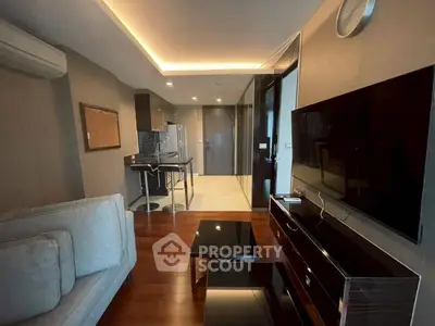 Modern living room with sleek design and open kitchen layout, featuring a large TV and stylish furniture.
