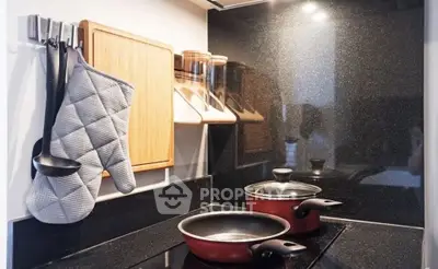 Modern kitchen with sleek black countertops and red cookware, featuring a stylish backsplash and organized storage.