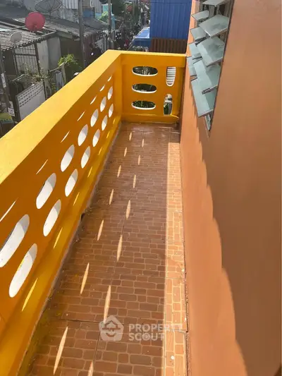 Charming narrow balcony with vibrant yellow railing and terracotta tiles, perfect for urban living.