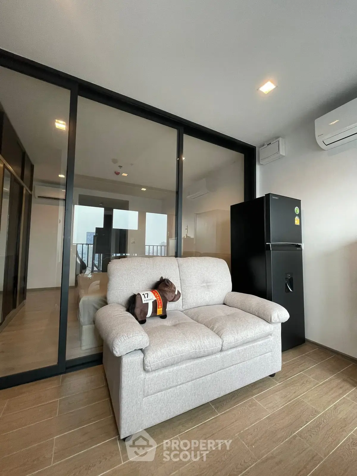 Modern apartment interior with cozy sofa and sleek black refrigerator, featuring glass partition and wooden flooring.
