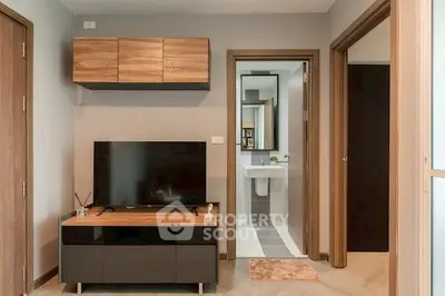 Modern living room with sleek TV stand and wooden cabinets, adjacent to a bathroom entrance.