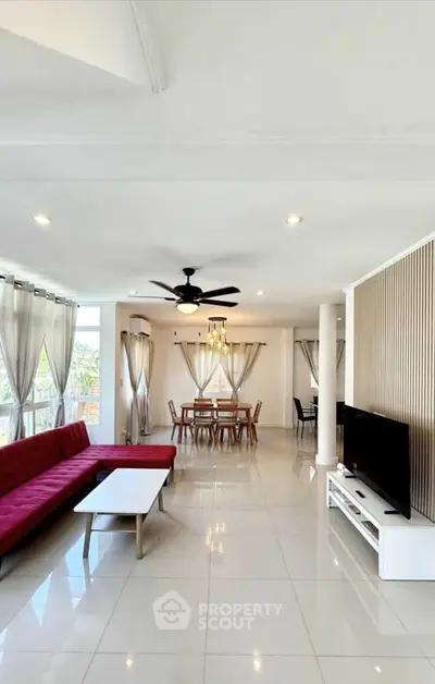 Spacious modern living room with red sofa and dining area, featuring elegant curtains and ceiling fan.
