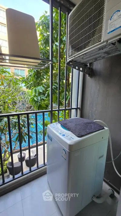 Charming balcony with washing machine overlooking lush greenery and pool view.