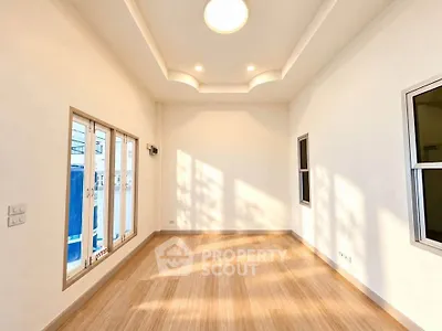 Spacious empty room with wooden flooring and large windows, perfect for customization.