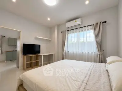 Spacious bedroom with modern decor and natural light, featuring a comfortable bed and a flat-screen TV.