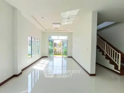Spacious sunlit living room with large windows and modern staircase in a contemporary home.