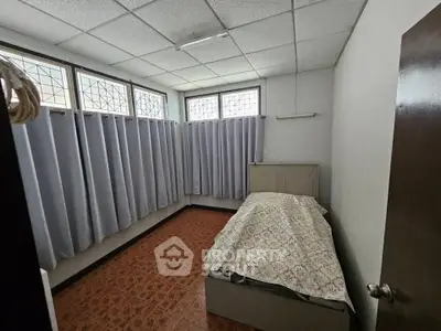 Cozy bedroom with natural light and tiled flooring, featuring a single bed and ample window space.