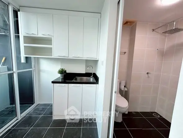 Modern bathroom with sleek black tiles and white cabinetry, featuring a spacious shower area.