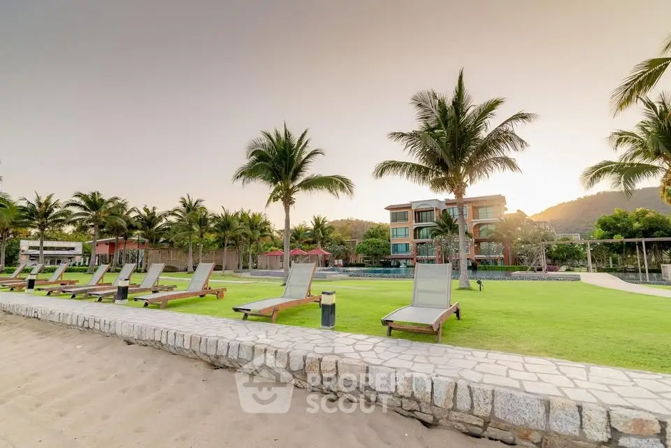 Luxurious beachfront property with palm trees and sun loungers at sunset.