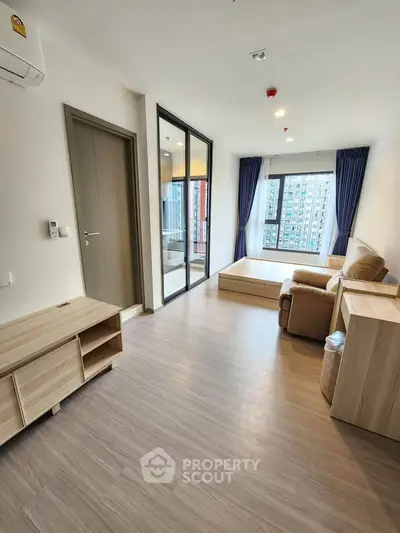 Modern living room with large windows and city view, featuring wooden flooring and cozy furniture.