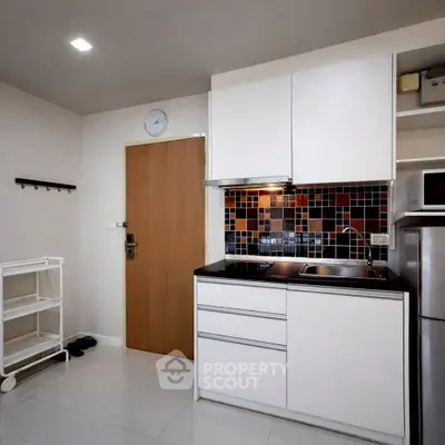 Modern kitchen with sleek white cabinets and colorful backsplash in a compact apartment.